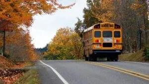 Yellow school bus driving along a paved Massachusetts road during the autumn back-to-school season