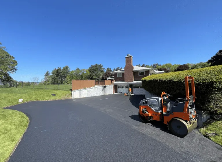 Hamm compaction roller parked on a freshly paved asphalt driveway in front of a brick home in Hardwick MA by Blacktop Services.
