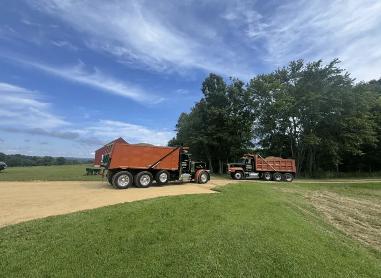 Heavy-duty dump trucks preparing aggregate base material for an asphalt paving project in Hubbardston MA by Blacktop Services.