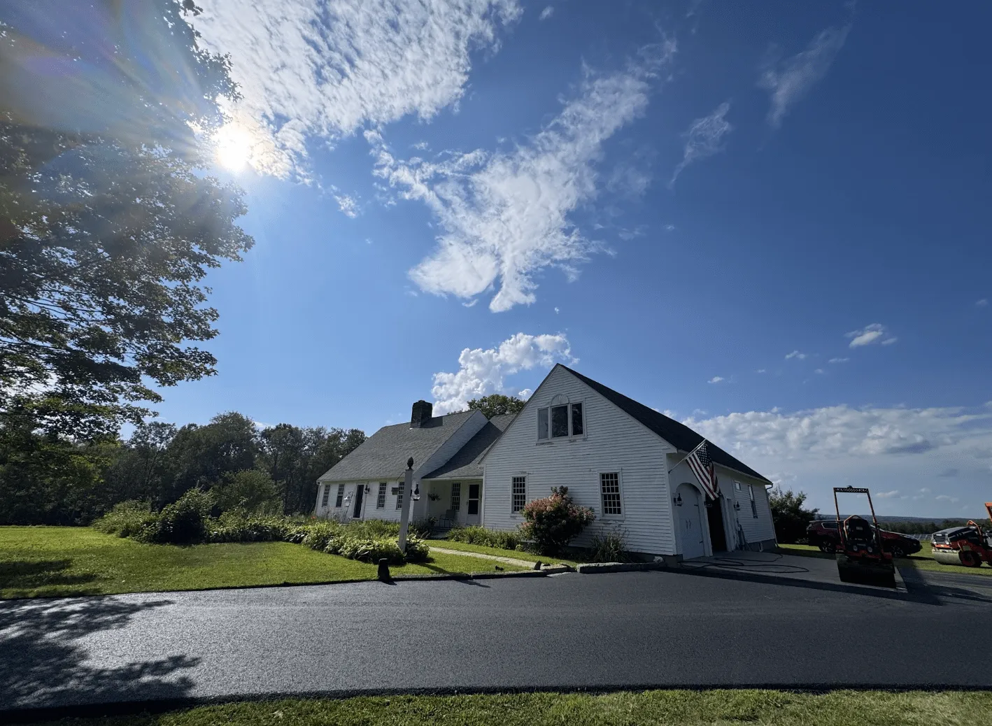 Freshly paved blacktop driveway in front of a white residential house with compaction roller equipment on site in Hubbardston Massachusetts.