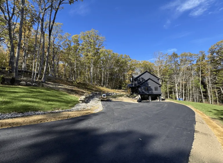 Newly paved curved asphalt driveway leading to a modern black home in Petersham MA by Blacktop Services.