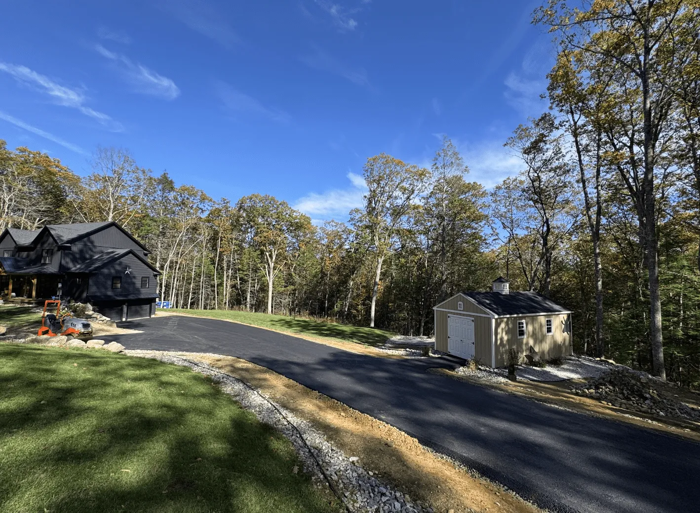 Long residential blacktop driveway passing a outdoor shed toward a home in Petersham Massachusetts paved by Blacktop Services.