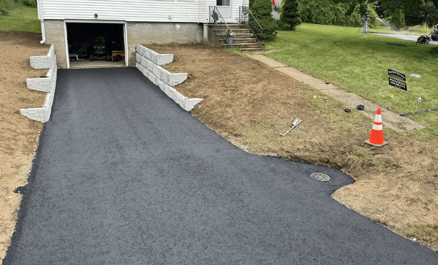 Freshly paved asphalt residential driveway with newly installed stone retaining walls by Blacktop Services in Barre MA
