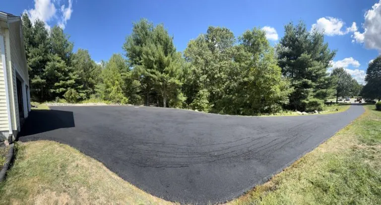 Wide panoramic view of a newly paved asphalt driveway and parking area next to a home