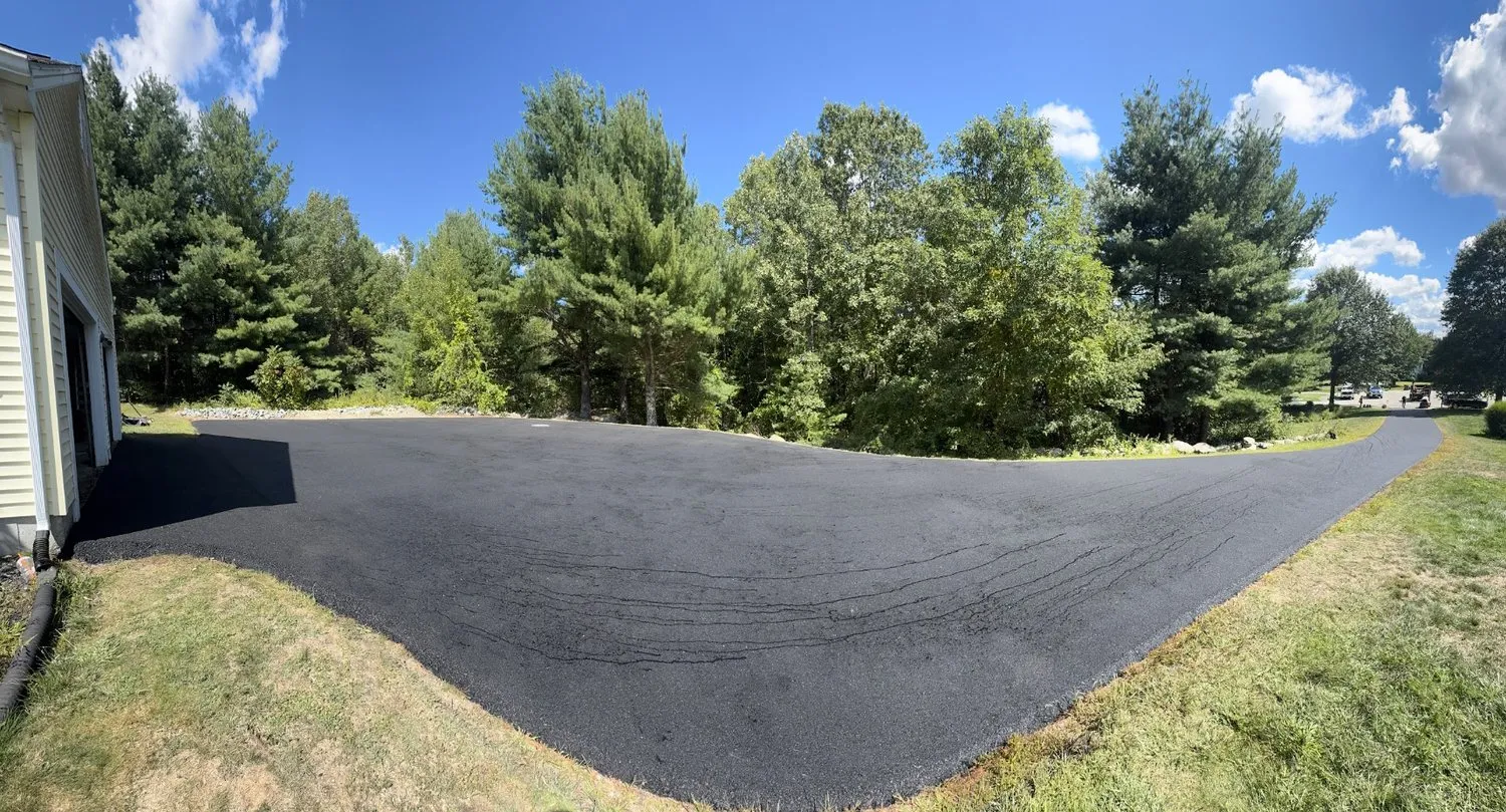 Wide panoramic view of a newly paved asphalt driveway and parking area next to a home